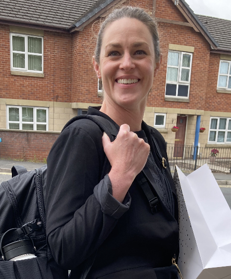photo of Staci (light-skinned woman) smiling and carrying a backpack and shopping bag