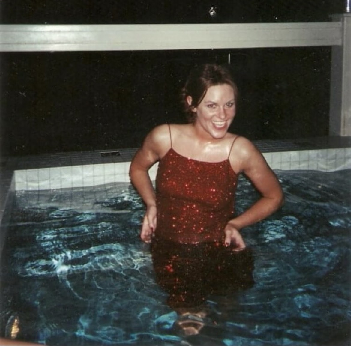 Photo of Staci (light-skinned woman) wearing a red sequined cocktail dress and standing in a hot tub